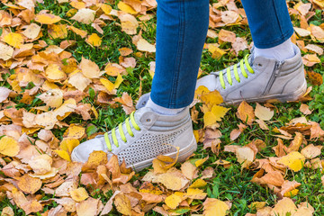 Legs of a child with sports sneakers and green laces for running on yellow leaves on an autumn day.