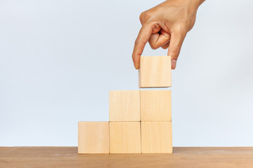 Hand arranging wooden cube stack a staircase on white background. Concept of success, winner, victory or top ranking