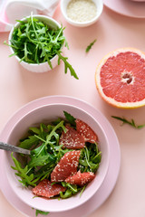 Fresh citrus salad with arugula, grapefruit and sesame seeds on pink background. Selective  focus. Raw vegetarian spring detox food.
