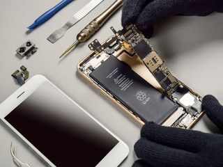 Technician or engineer disassembling components broken smartphone and take off logic board for repair or replace new smartphone logic board on desk 