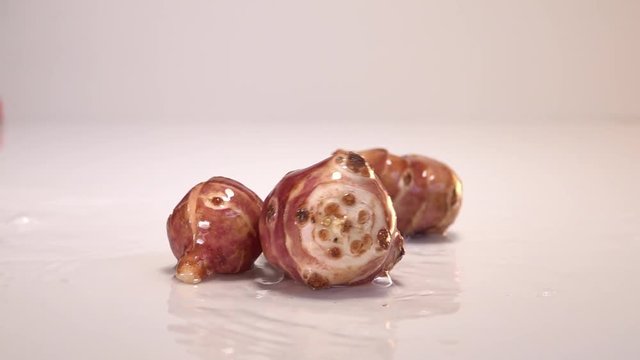 Jerusalem artichoke falling in water on white table in white background. Slow Motion 240 fps