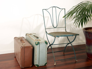 Two old retro suitcases, vintage metal lawn chair, wooden floor and a white stucco background
