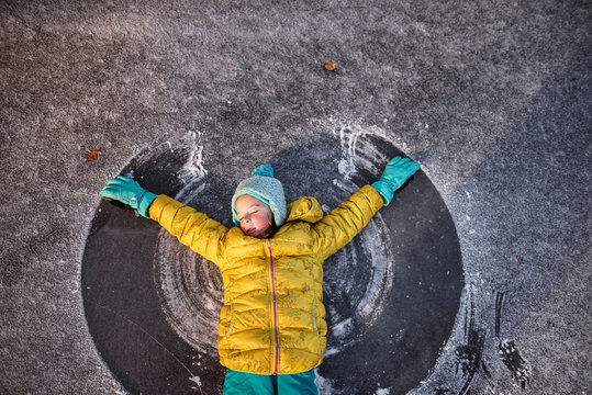 Girl lying on a frozen pond making a snow angel with her arms, United States