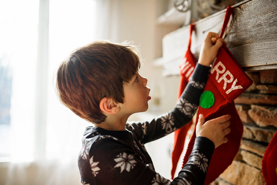 Boy hanging Christmas stocking on fireplace at home