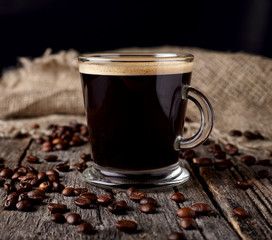 Coffee in the glass cup with coffee beans  on the wooden background.
