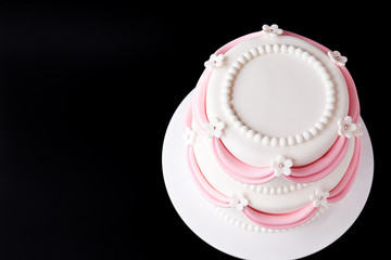 White wedding cake with pink elements made from pastry mastic on a black background. Top view. Sugar flowers, marzipan flowers and mastic, beautiful decor for decorating cakes. Close-up.