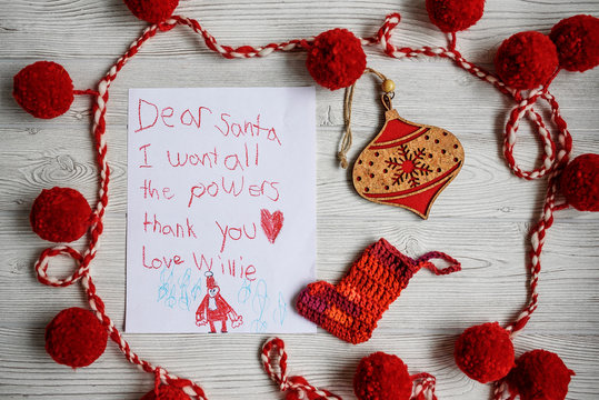 Overhead view of a child's letter to Santa Claus asking for superpowers on a table with assorted Christmas decorations