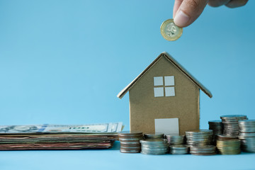 hand putting coin to House model around with stacking coins money on blue background. Saving and investment to real estate concept. -image.