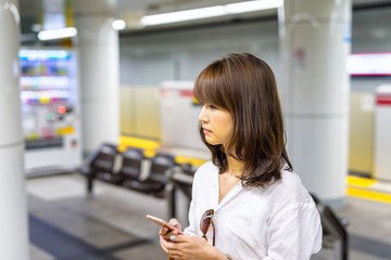 Japanese girl with smartphone waiting on the subway platform