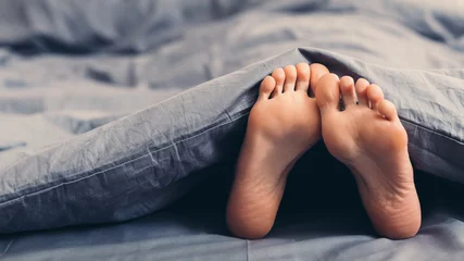 Foto op Canvas Female beautiful feet under blanket in bed © Prostock-studio