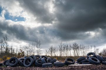 Old rubber tires dumped and polluting nature, dark cloudy sky background
