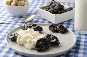 Closeup of plate with cottage cheese. prunes, peanuts on table. Delicious dieting dinner served on blue checkered tablecloth