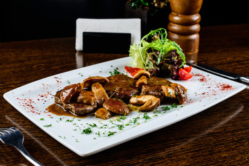 Appetizing mushrooms baked in sauce, served with tomatoes and parsley in the white plate