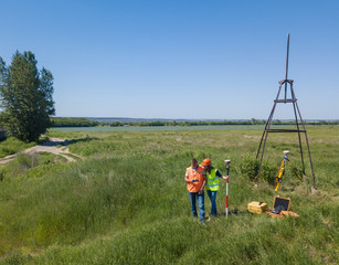 Two Land Surveyors Engineers are Working on the Green Field. Male and Female Surveyors on a Construction Side. View From Above..