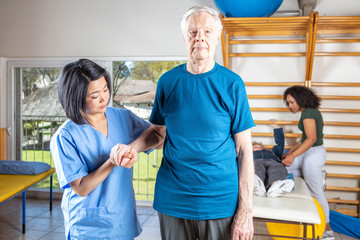 Nurse helping elderly man in a rehab gym