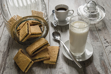 biscotti farciti al cioccolato fondente con tazzina da caffè e bicchiere latte