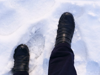 Person's feet in leather boots walking in the snow in winter