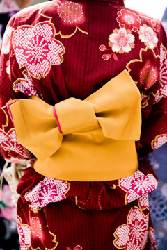Detail of woman wearing red/maroon flower patterned summer kimono "yukata"  with bright orange &ldquo;obi&rdquo; belt.