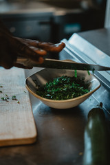 Hands of black cook pouring rubbed fennel into a plate with a big knife, professional kitchen of a vegetarian healthy restaurant