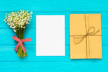 Bouquet of lily of the valley and empty paper sheet on table, top view, space for text, flat lay.