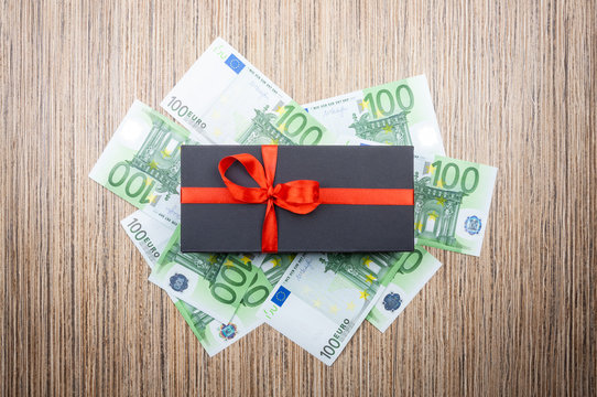Black gift box with a bow with euro banknotes on a wooden table. top view