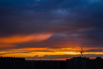 silhouette of construction crane and buildings against horizon of sunset sky