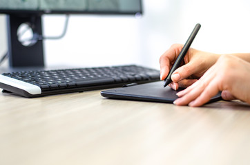 Closeup of female hands working with graphic tablet in front of a computer