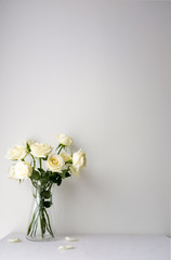 White roses in a glass vase on white table top on white background with copy space for product mockup placement for valentine's day wedding ceremony