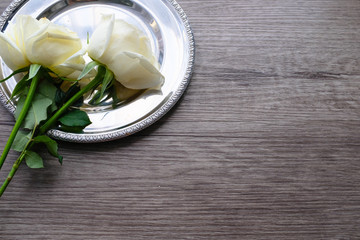 White roses on vintage round silver plate on wooden plank floor with copy space for valentine's day wedding ceremony