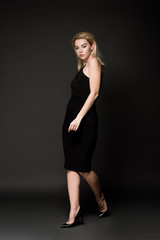 beautiful young woman in elegant black dress posing on black