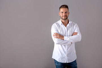 A smiling handsome young man in a white shirt standing in front of a grey background in the studio.