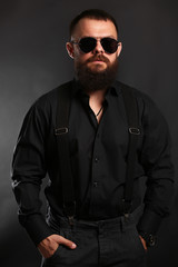 young handsome man with big beard and black sunglasses on black background  close up portrait 