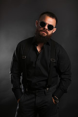 young handsome man with big beard and black sunglasses on black background  close up portrait 