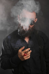 young handsome man with big beard and black sunglasses on black background  smoking cigar 