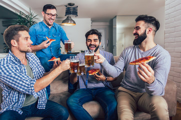 Group of four male friends drinking beer and eating pizza at home.