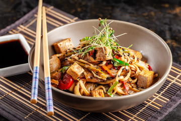 The concept of Japanese cuisine. Chinese noodles with chicken, grilled vegetables, and tofu in unagi sauce. Serving Asian dishes in the restaurant in a plate on a bamboo mat. Top view, copy space