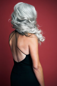 Beautiful woman wearing a black evening dress with long, silvery, grey hair, back view.