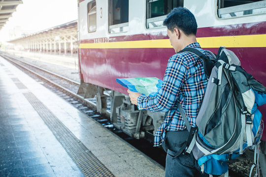 Young asian man look at the map for planning for travel by train on holiday and weekend at Hua lum phong Bangkok train station, Thailand. Man and backpacker travel concept in Thailand