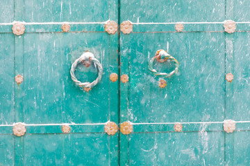 Background of blue color. An iron door with the forged round handles in the form of rings against the background of the falling snow