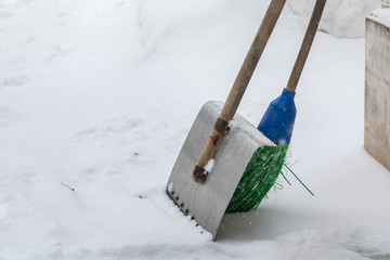 Shovel for cleaning of snow and a broom stand on the street in snowfall. Municipal services clean...