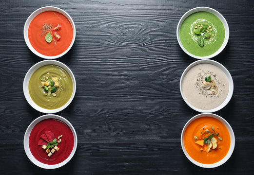 Various soups in bowls and space for text on wooden background, top view. Healthy food