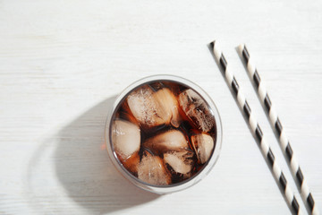 Glass of refreshing cola with ice cubes on white wooden background, top view