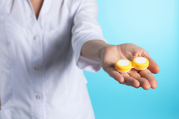 Female doctor holding contact lens case on color background, closeup. Medical object