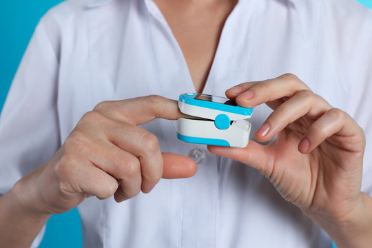 Female doctor holding pulsimeter on color background, closeup. Medical object