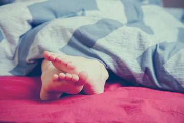 Feet under the blanket on bed on bedroom. Sleep and relax concept.