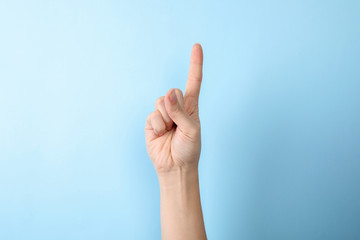 Woman showing number one on color background, closeup. Sign language