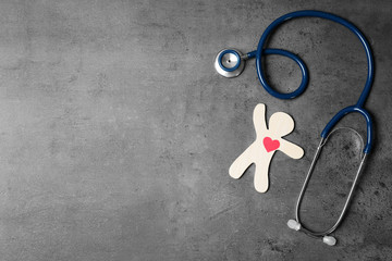 Stethoscope with human figure and heart on grey background, flat lay. Space for text