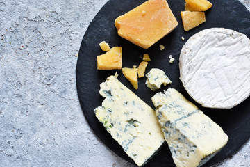 A set of cheeses: brie, blue cheese, parmesan, camembert on a slate board. Plate with delicacies. View from above