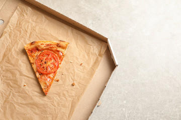 Last slice of cheese pizza in cardboard box on grey table, top view with space for text. Food delivery service