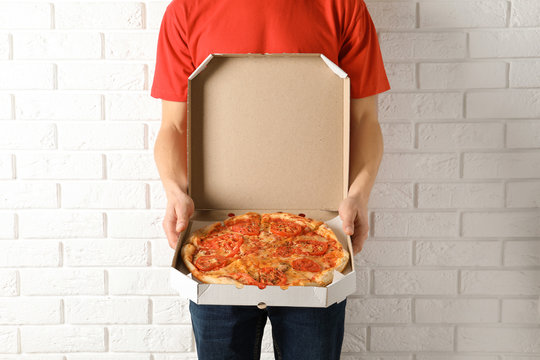Young man with opened pizza box near white brick wall. Food delivery service